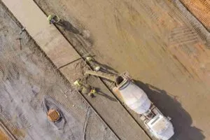 Workers pouring and smoothing a concrete slab under hot weather conditions on a construction site